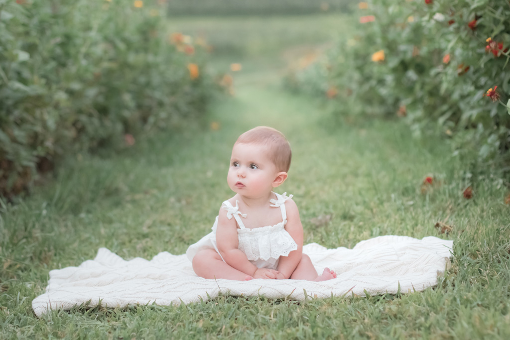 one year old girl in simmons flower field on cream blanket