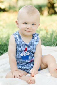 one year old boy in blue gingham romper sitting on cream blanket in simmons farm apple orchard