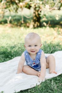 one year old boy in blue gingham romper sitting on ivory blanket in simmons farm apple orchard