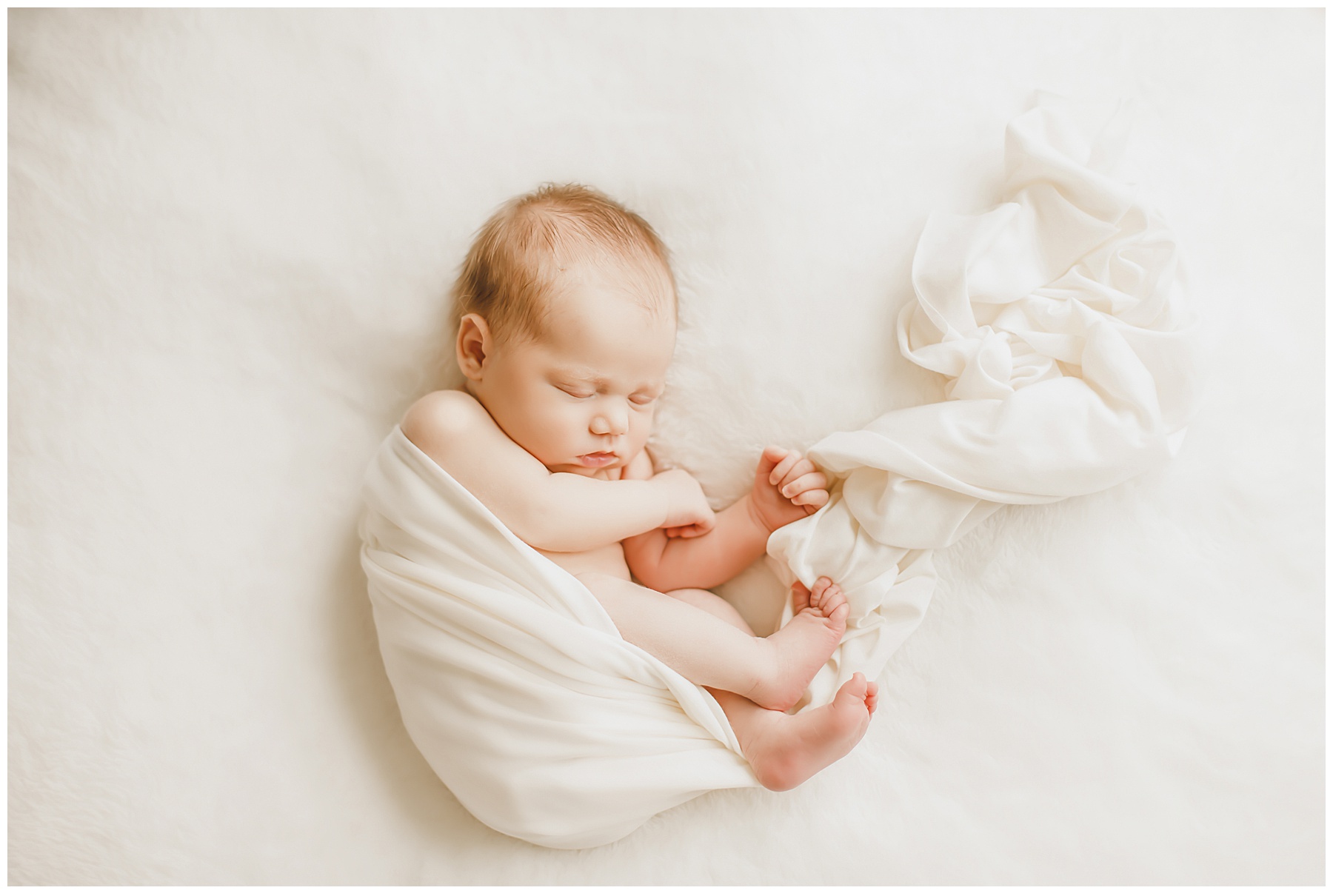 newborn baby wrapped in white wrap on white blanket