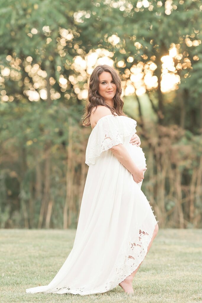 expecting mother in long cream dress standing in field at sunset_petite magnolia photography