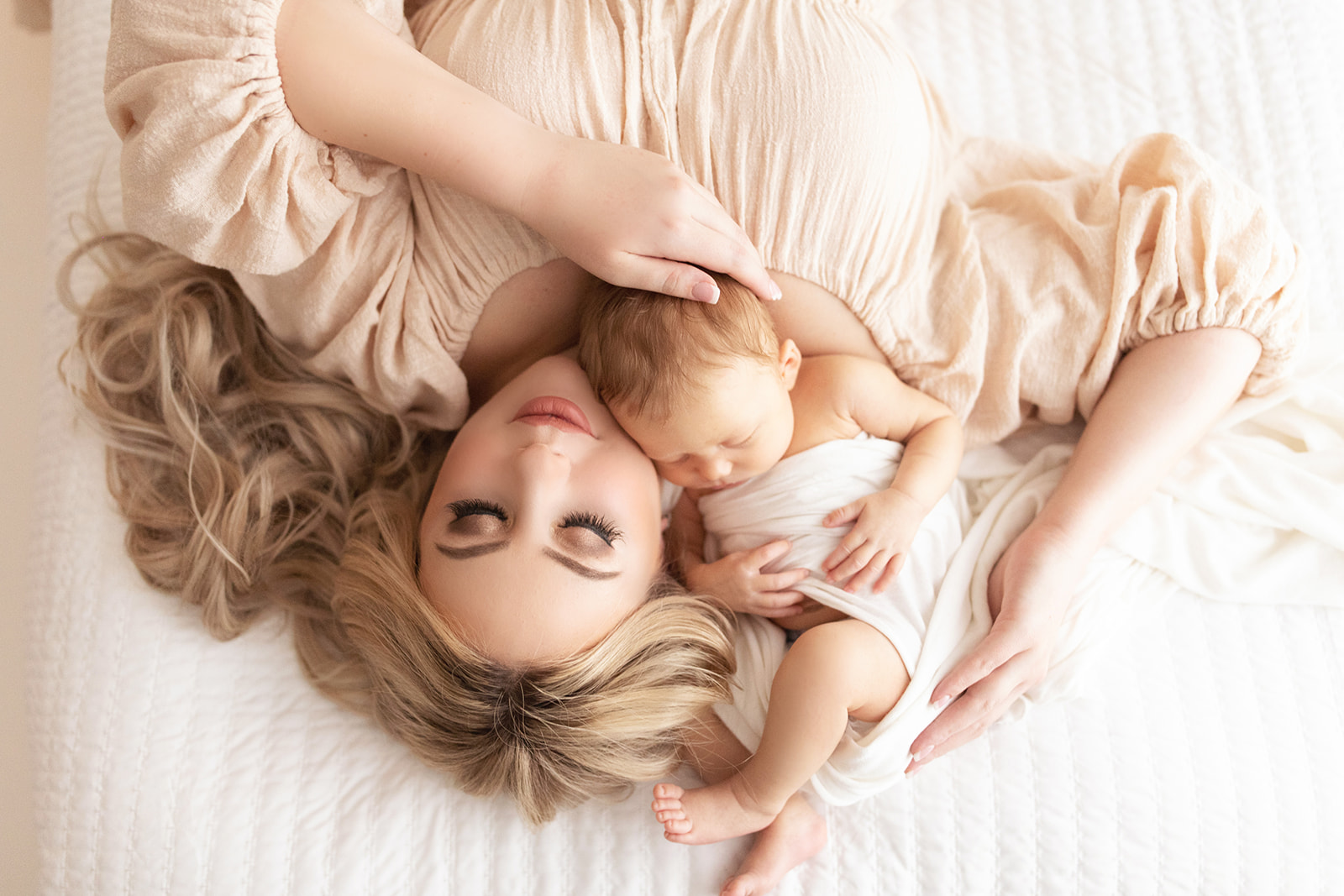 Mom wearing a beige dress cuddles with her newborn on a bed golden lotus doula services