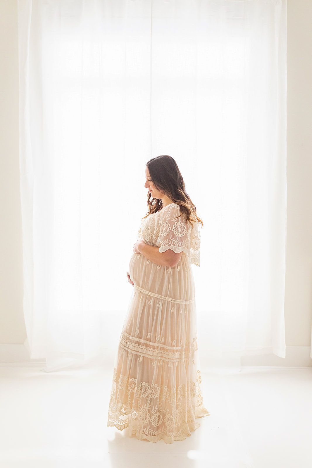 Mother to be stands in front of a large window in a maternity gown midwife center pittsburgh