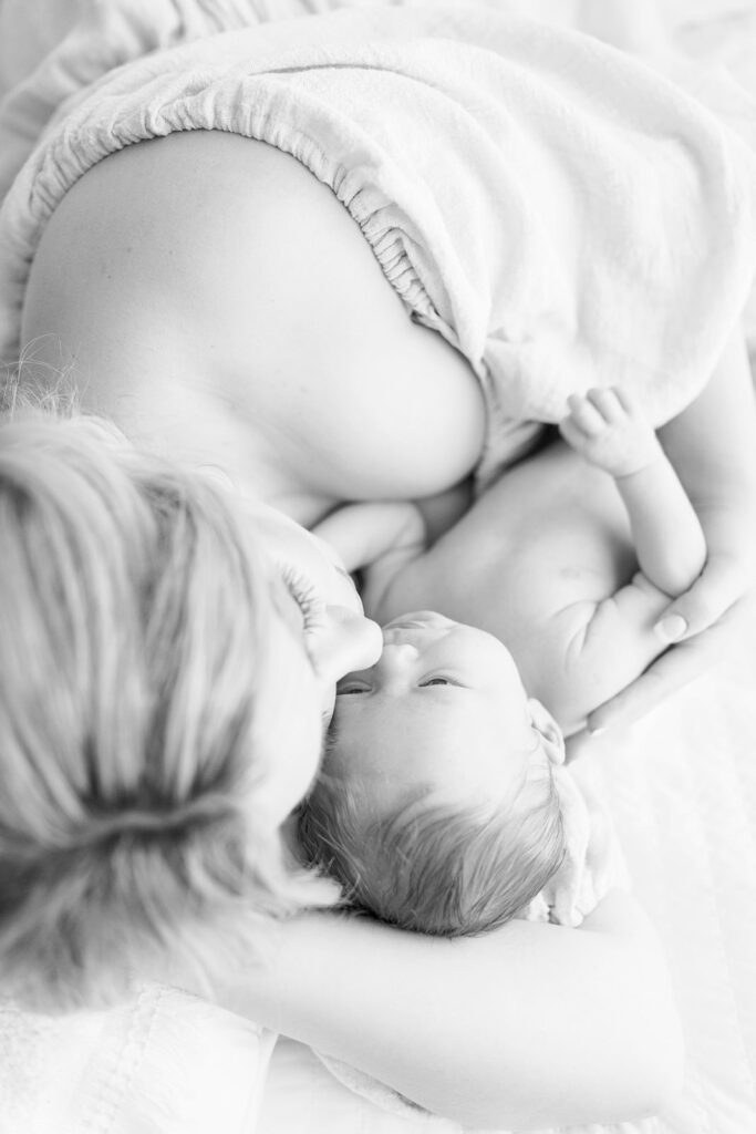 A mother in an off the shoulder dress cuddles with her newborn baby on a bed Precious and Posh