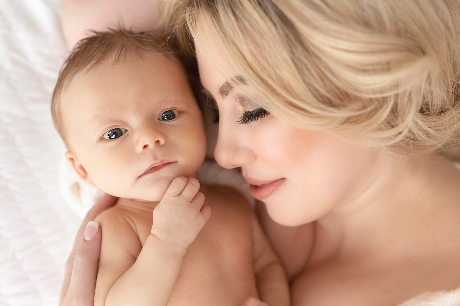 A mother cuddles with her newborn baby on a bed with eyes open Happy Baby Company