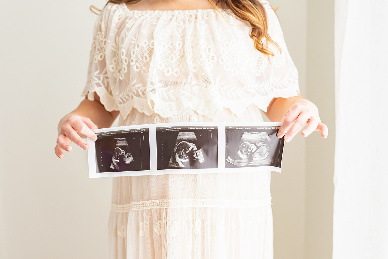 A mother to be holds her sonogram while wearing a lace maternity gown The Steel Orchid