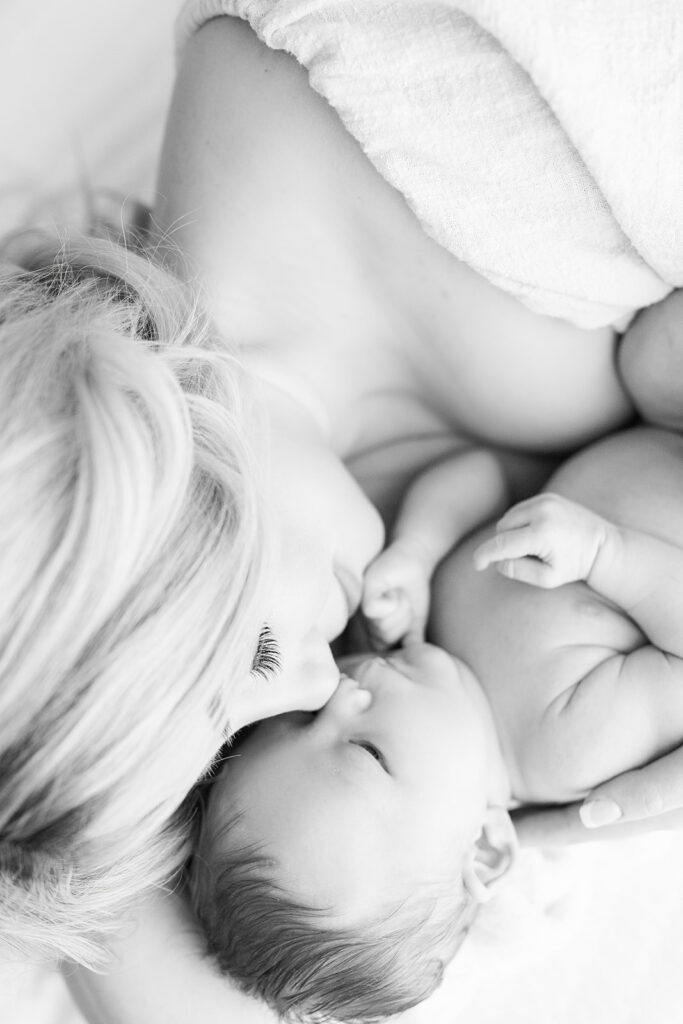 A mother presses her nose to her newborn baby's while snuggling on a bed Peek-A-View Baby