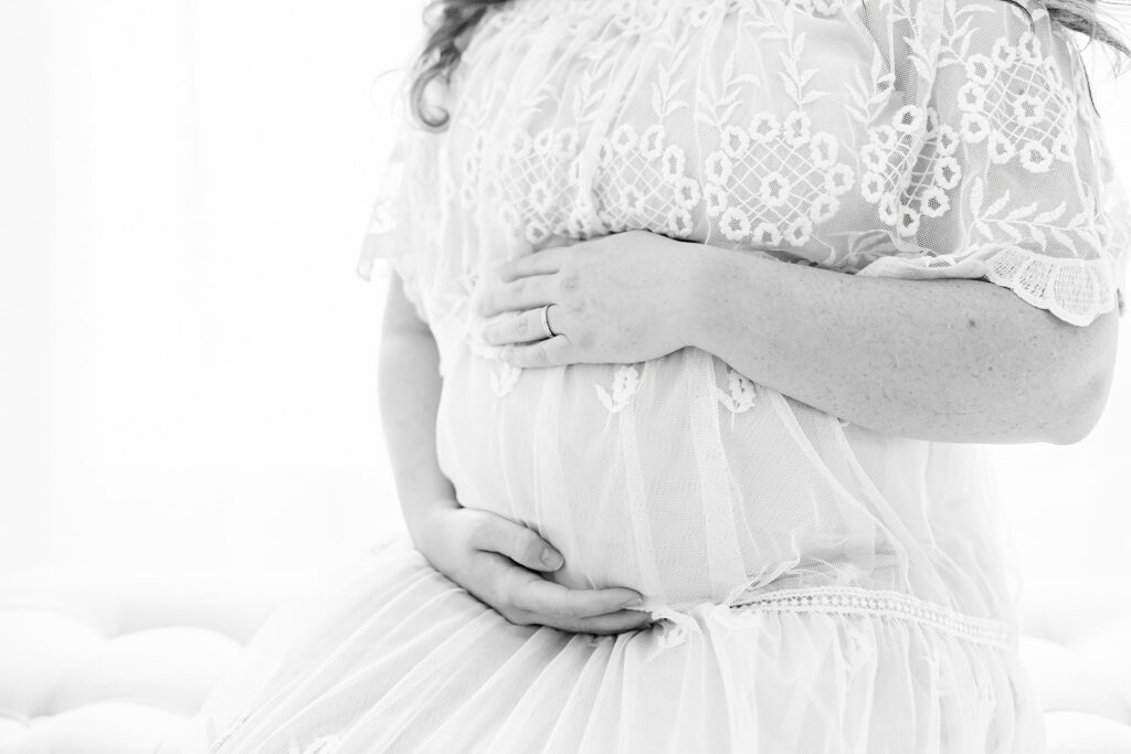 Details of a mother to be holding her bump in a white lace dress