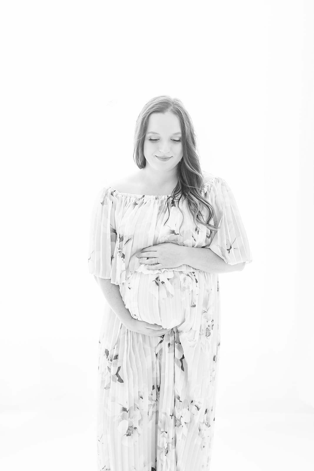 A mom to be stands in a studio in a floral pattern dress holding her bump