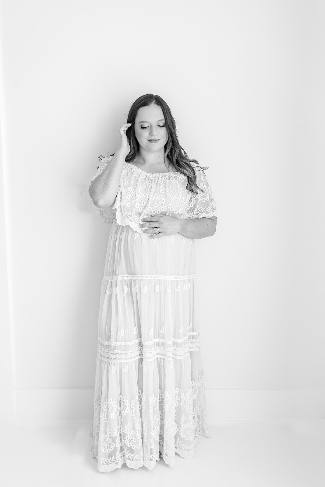 A mother to be stands in a studio fixing her hair in a white maternity dress Jefferson hospital labor and delivery