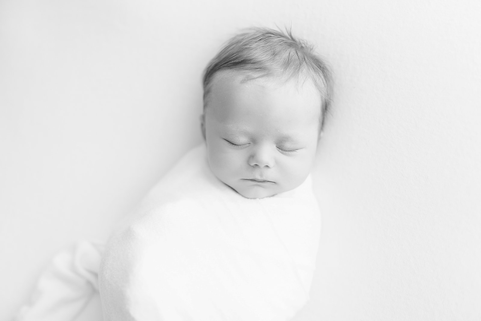 A newborn baby sleeps in a white swaddle