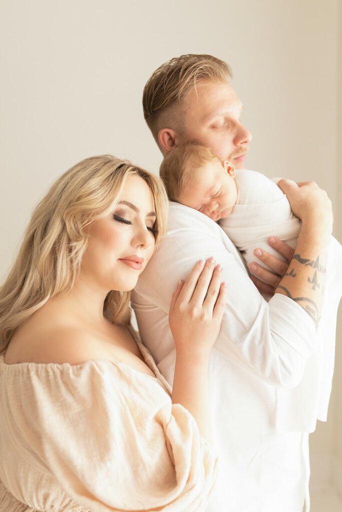 A new mom leans on the shoulder of dad as their newborn baby sleeps on his shoulder