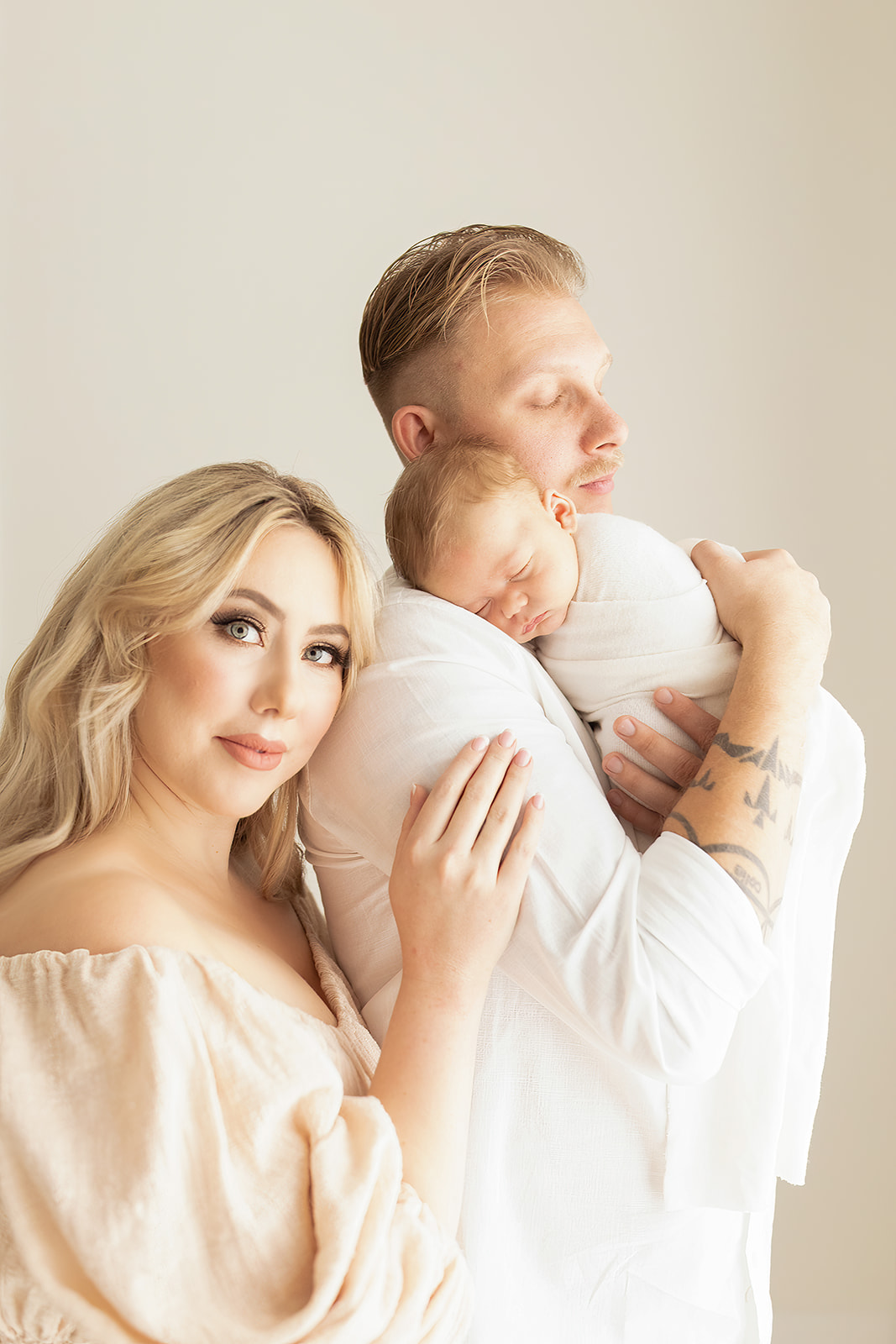 A new mom leans on the shoulder of her husband holding their sleeping newborn baby on his shoulder Noble Newborn