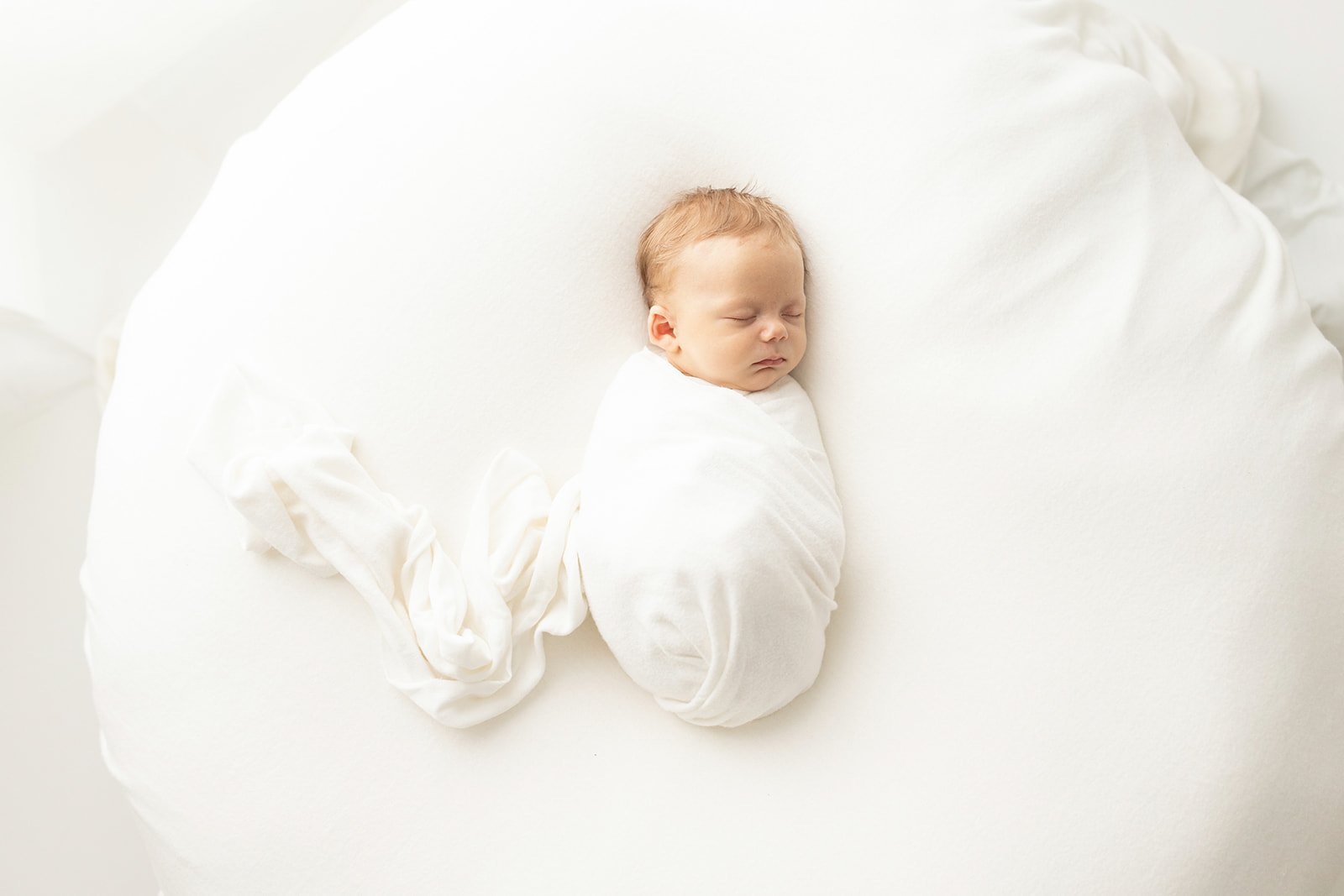 A newborn baby sleeps on a large cushion in a white swaddle Placenta Encapsulation Pittsburgh