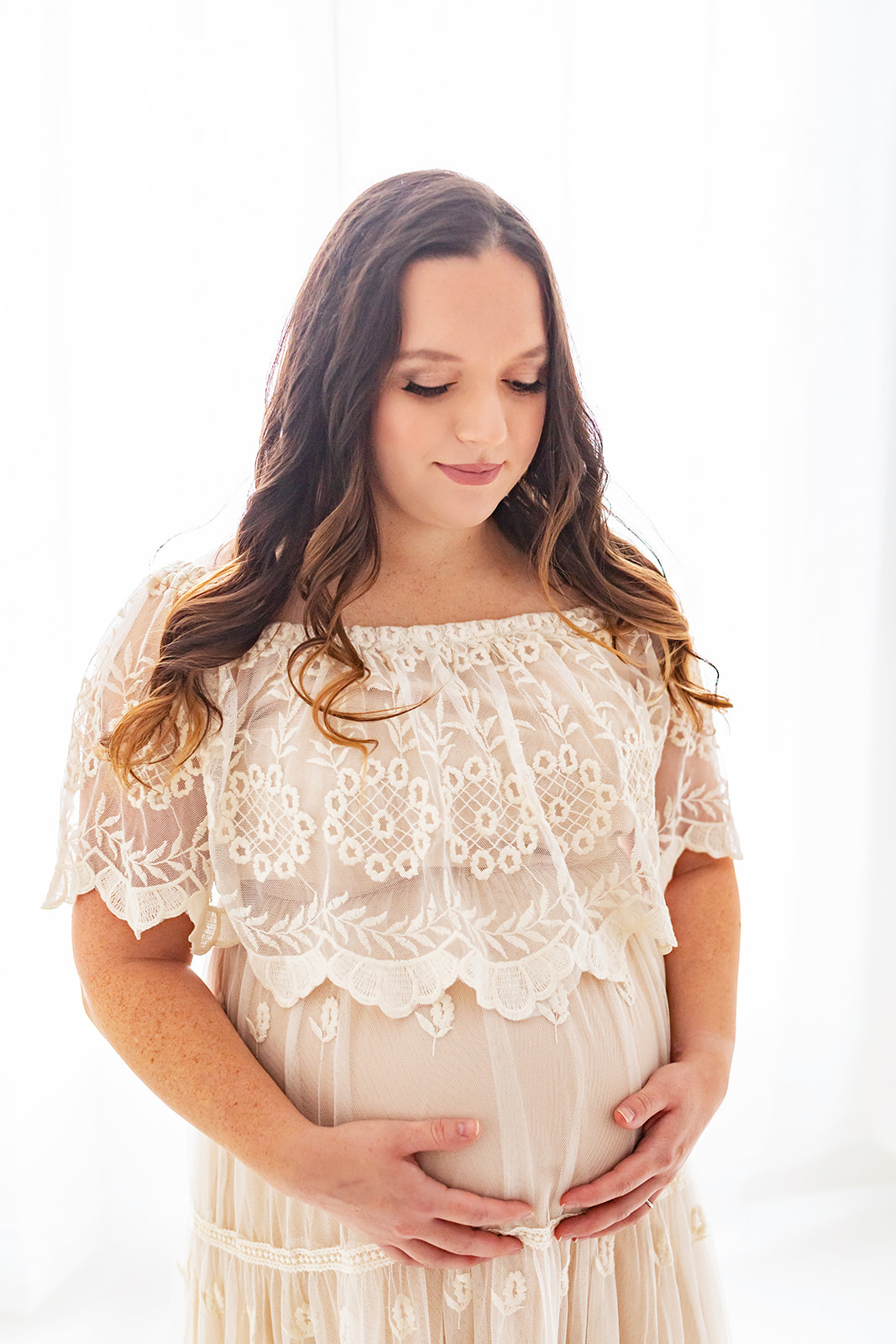 A mom to be wearing a lace tan maternity gown gazes down at her bump Prenatal chiropractor Pittsburgh