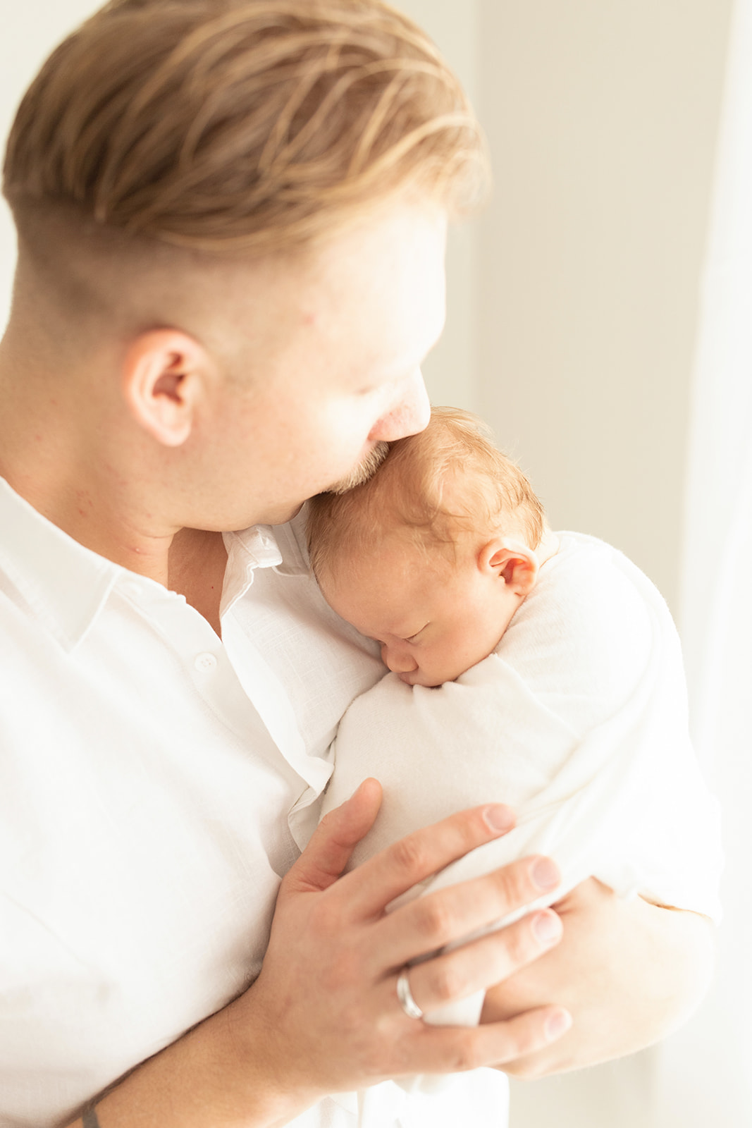 A new father cradles and kisses his sleeping newborn baby while standing in a window Infant CPR Classes Pittsburgh