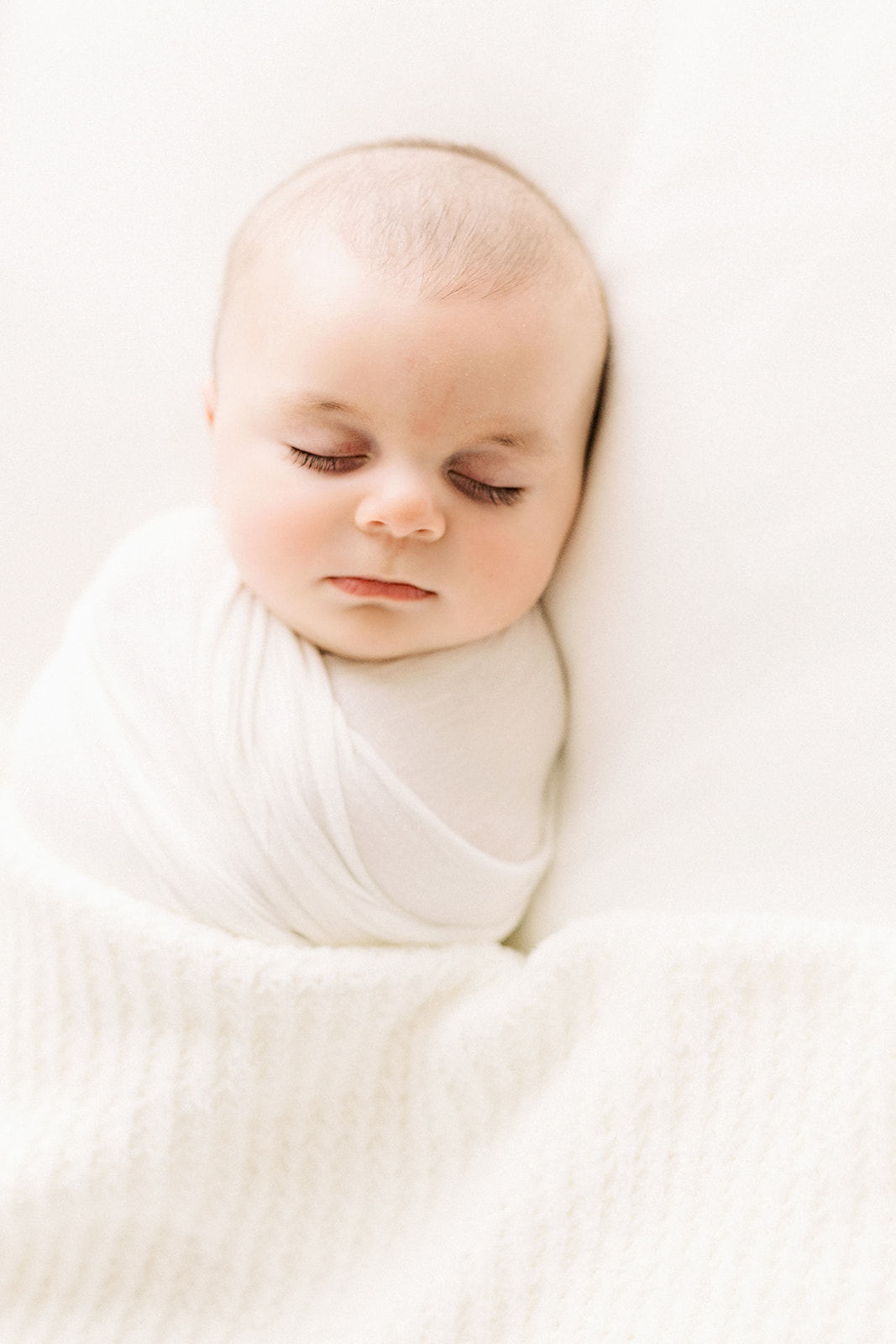 A newborn baby sleeps in a white swaddle in a studio thanks to baby sleep consultant pittsburgh