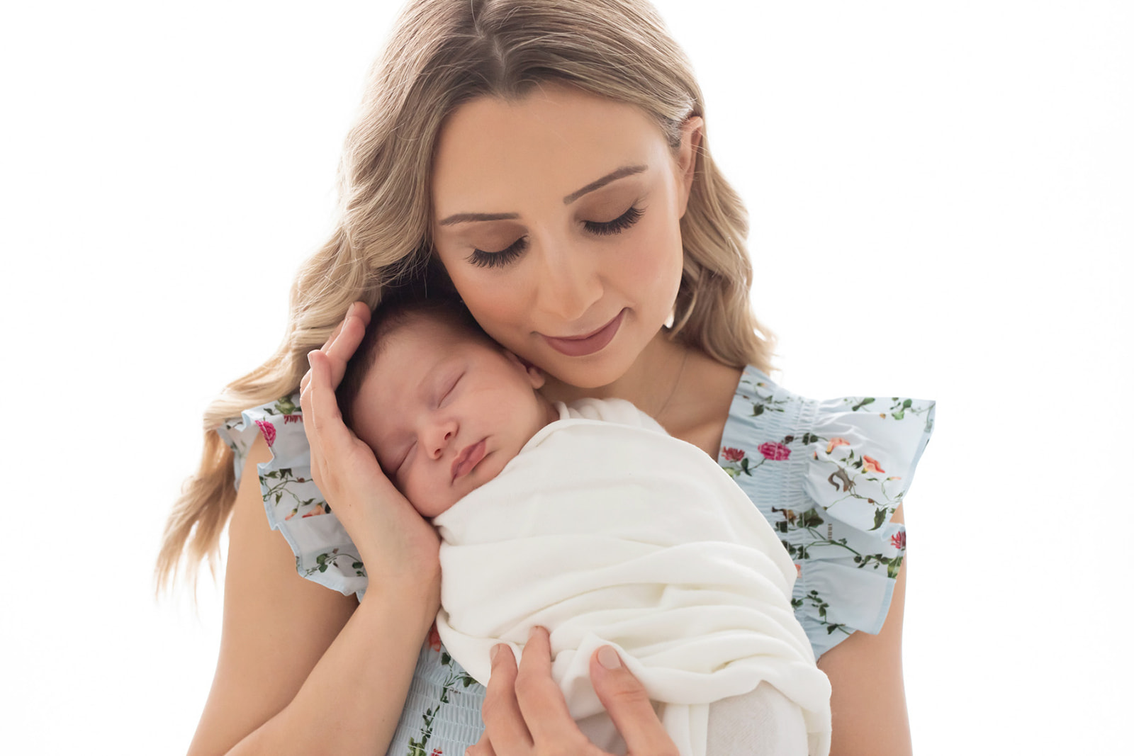 A new mom cradles her sleeping newborn baby against her chest while wearing a blue dress