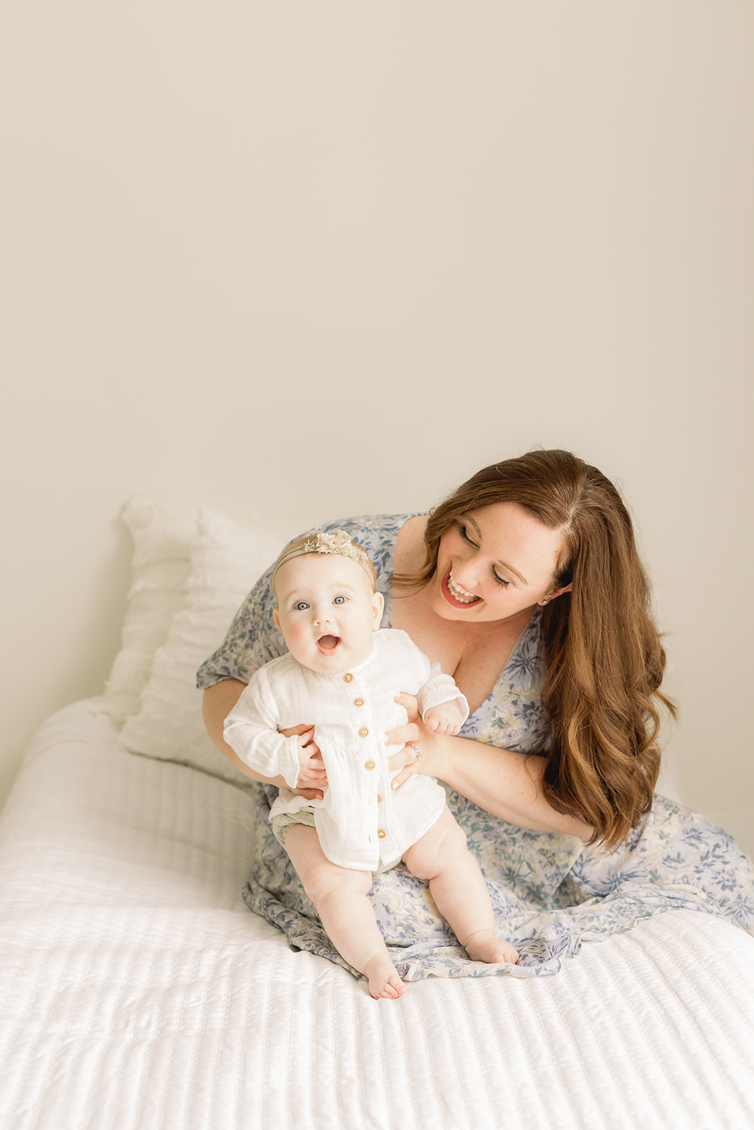 A mom plays with her infant daughter while sitting on a bed