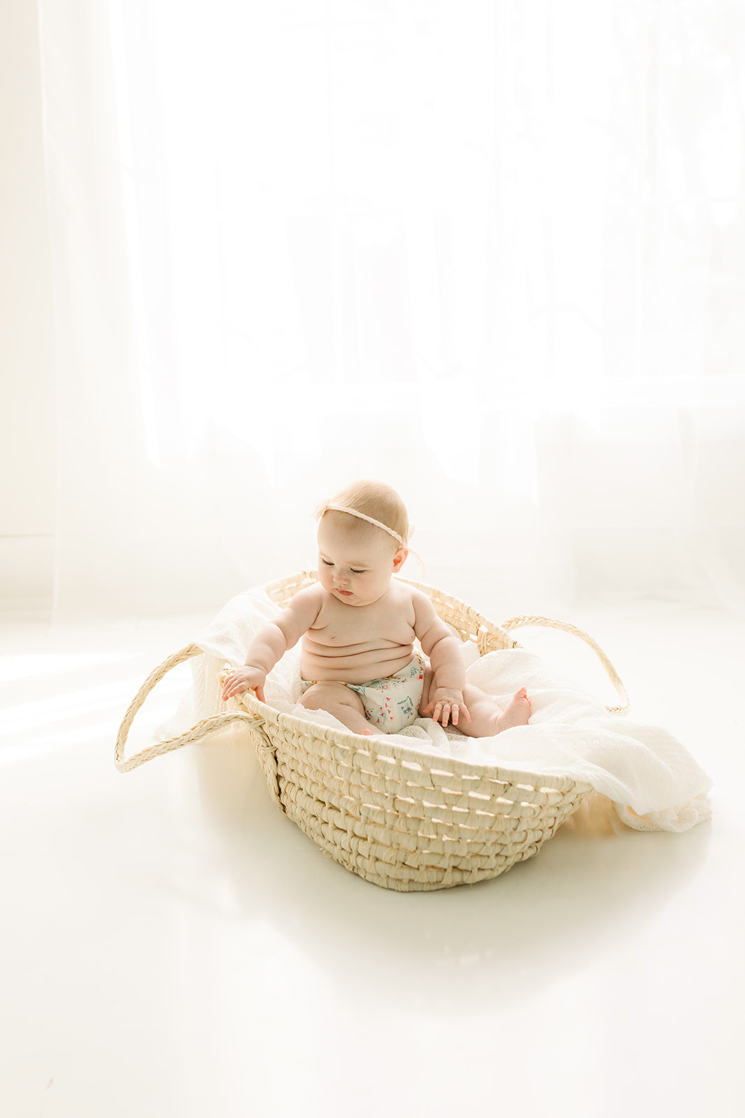 An infant sits in a woven basket in a studio wearing only a diaper before visiting a indoor playground pittsburgh
