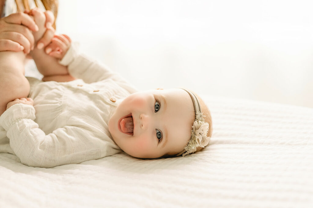 A newborn baby smiles while laying on a bed in a studio in a white dress at indoor playground pittsburgh