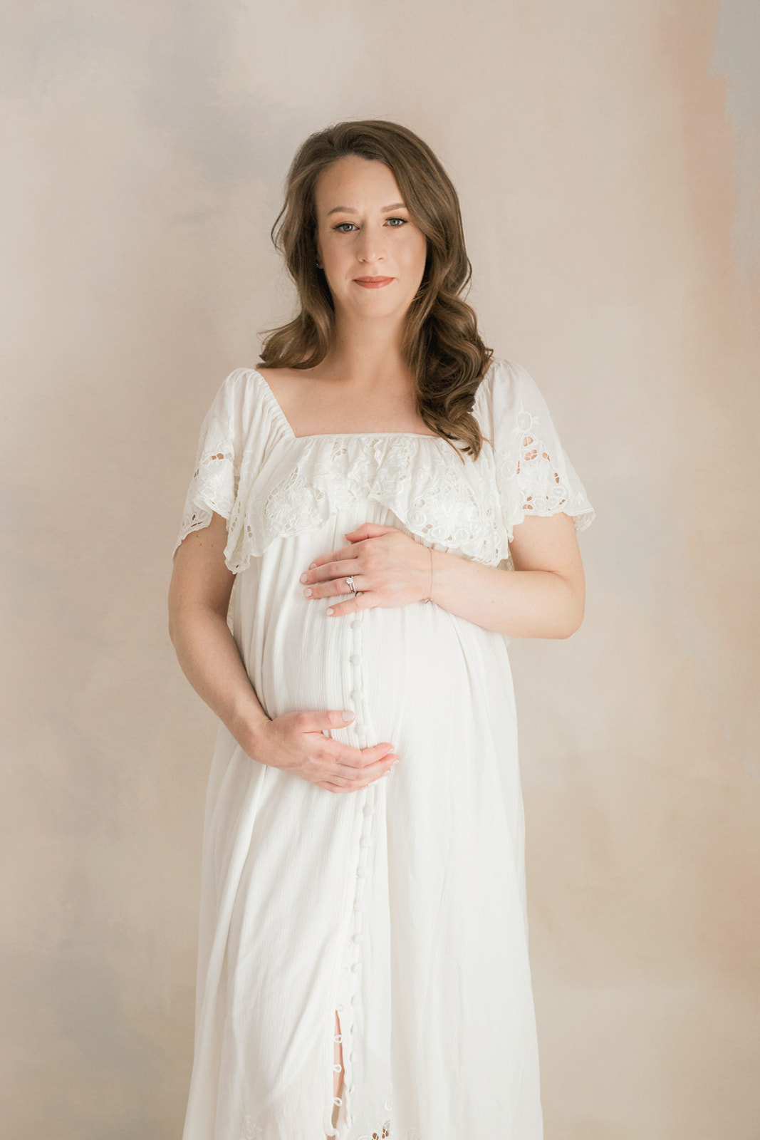 A mom to be in a white maternity gown stands in a studio holding her bump thanks to IVF Pittsburgh