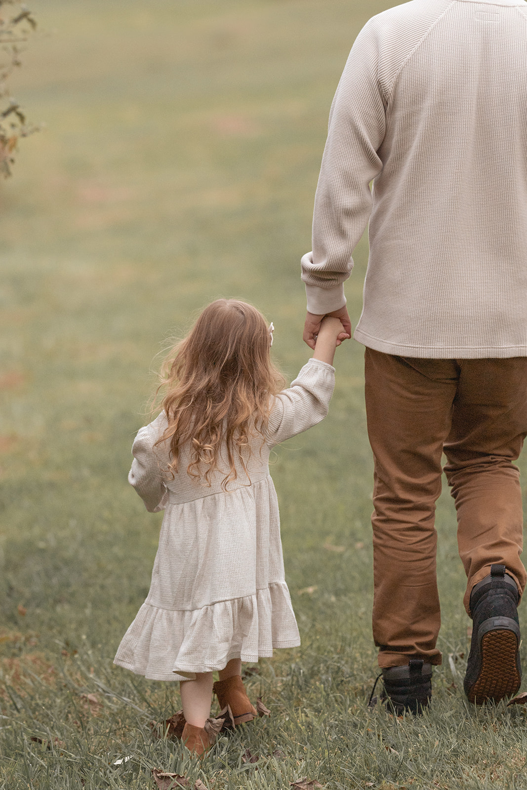 A young girl in a white dress walks with her dad holding hands through a grassy field after Montessori preschool Pittsburgh