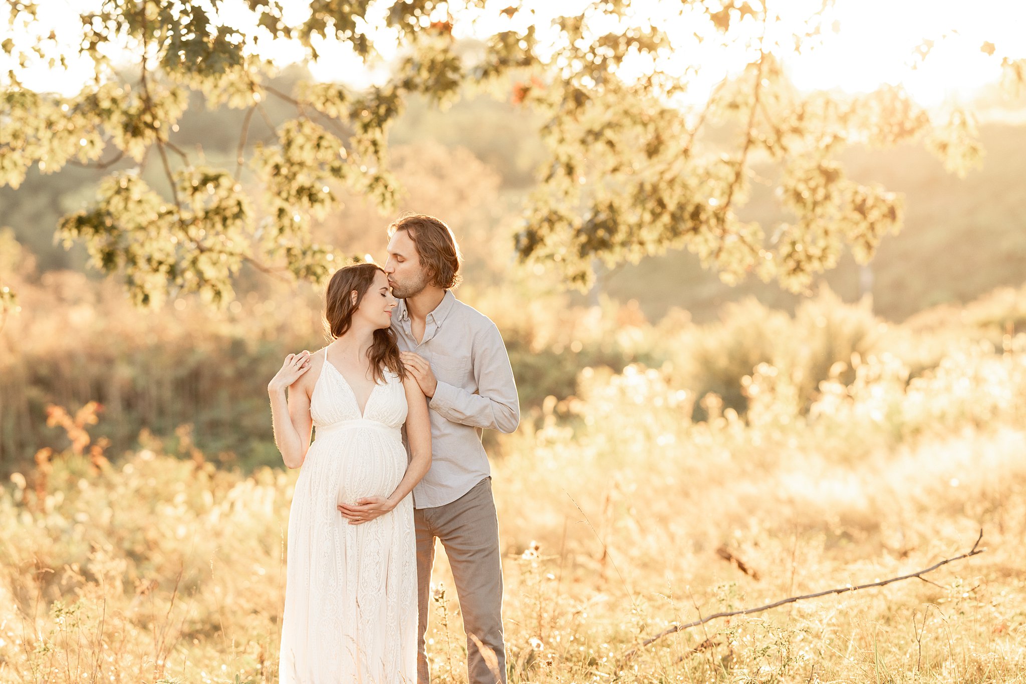 A dad to be kisses the forehead of his pregnant wife as they stand under a tree at sunset after getting a pittsburgh 3d ultrasound