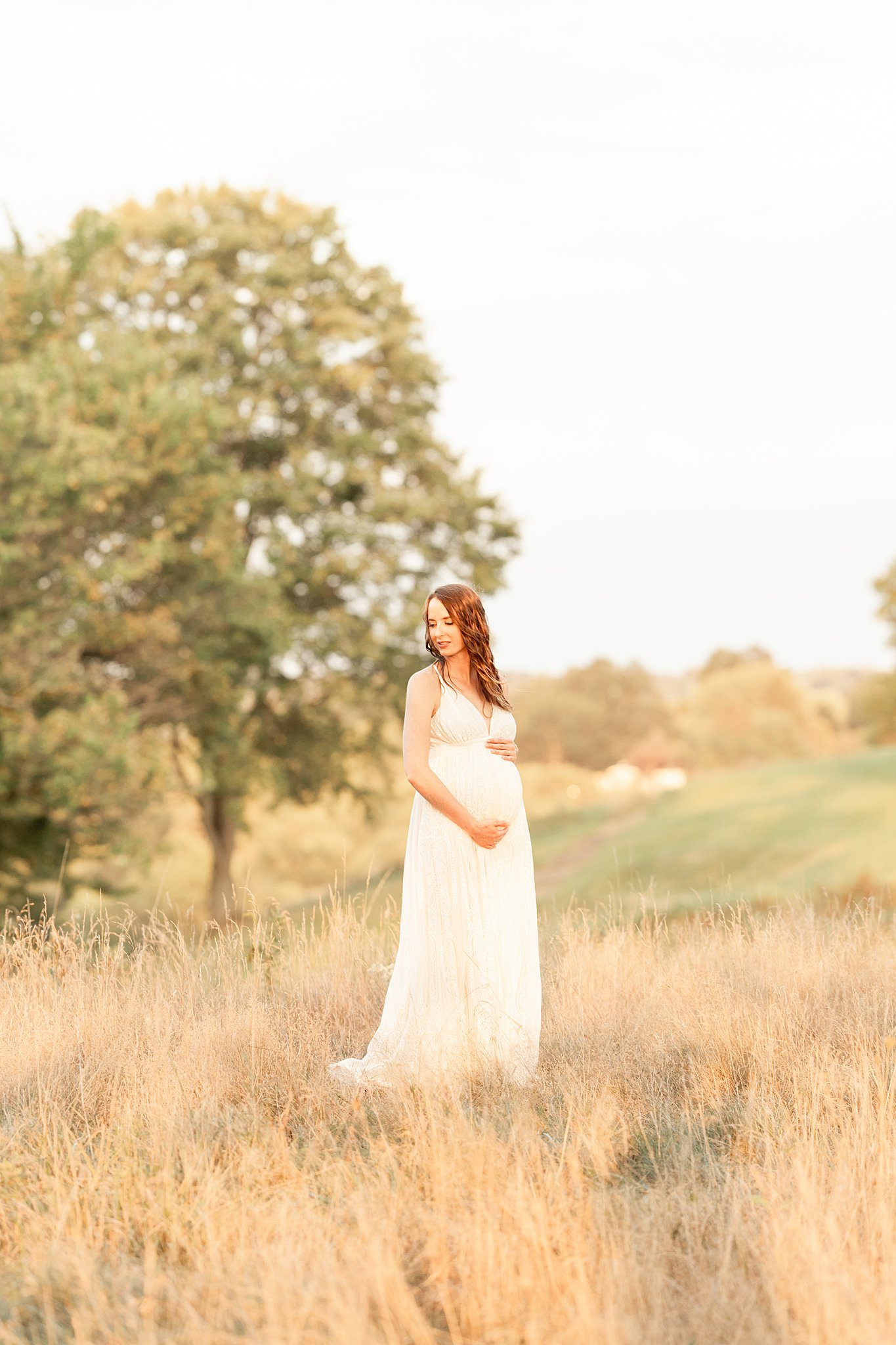 A mom to be smiles down her shoulder while standing in a field of golden grass and holding her bump after getting a pittsburgh 3d ultrasound