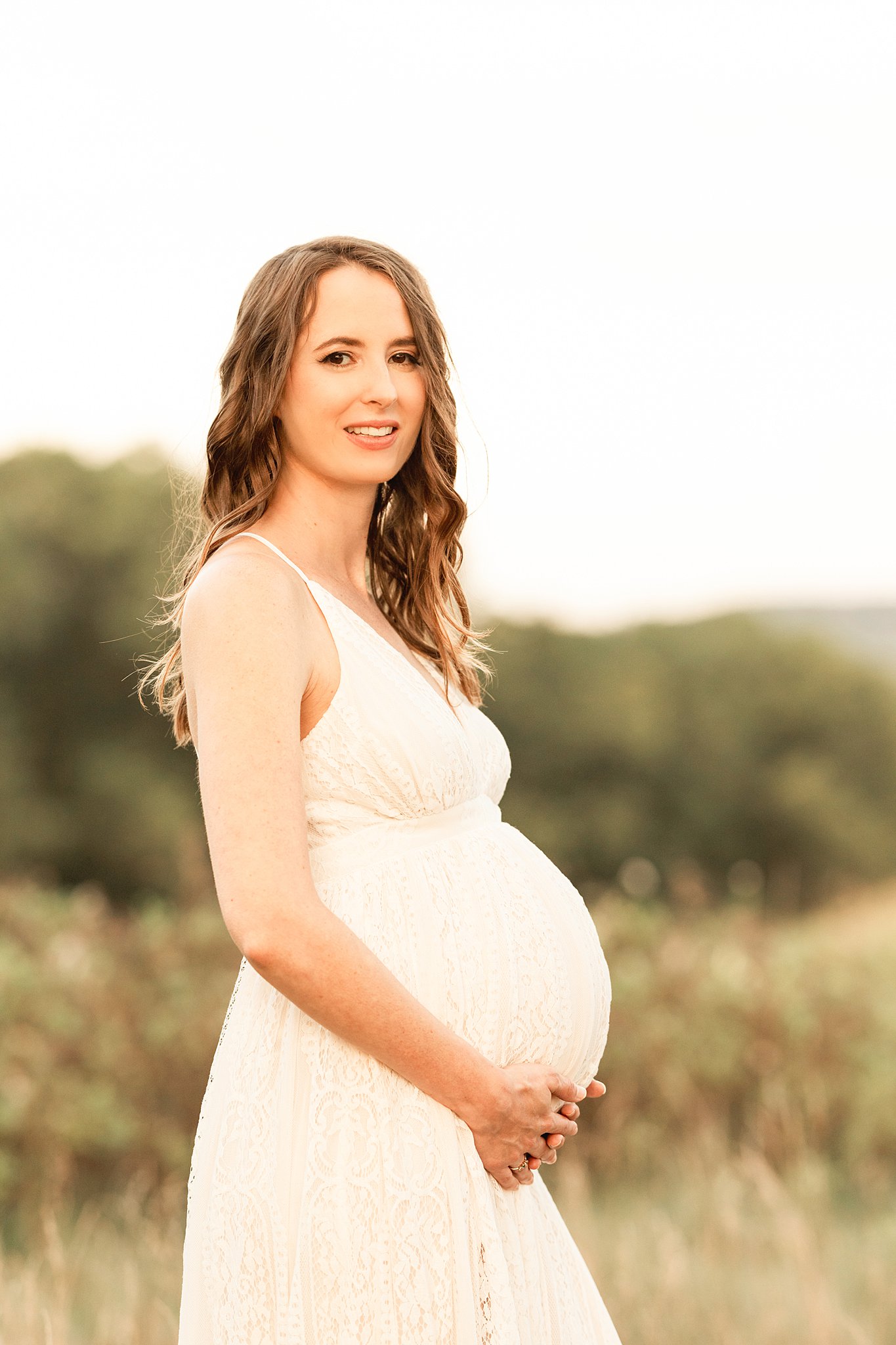 A mom to be in a white lace dress stands in a field of grass holding her bump after getting a pittsburgh 3d ultrasound