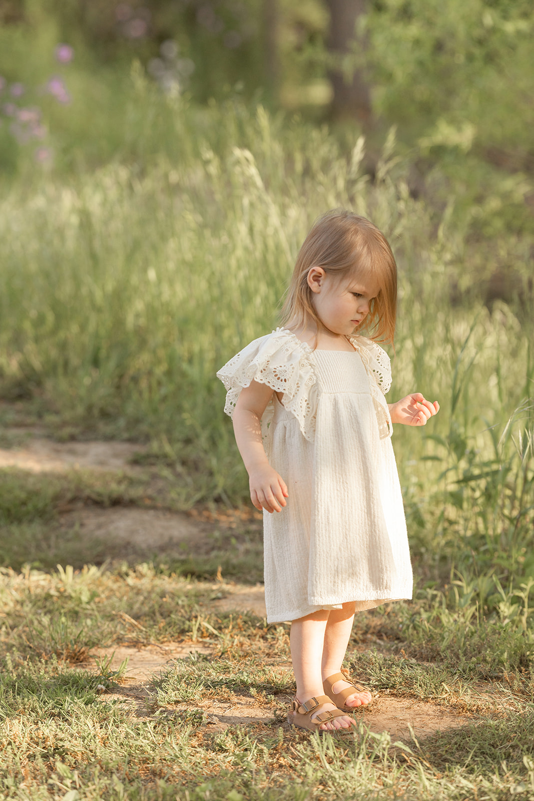 A young girl walks down a park trail lined with tall grass in a white dress
