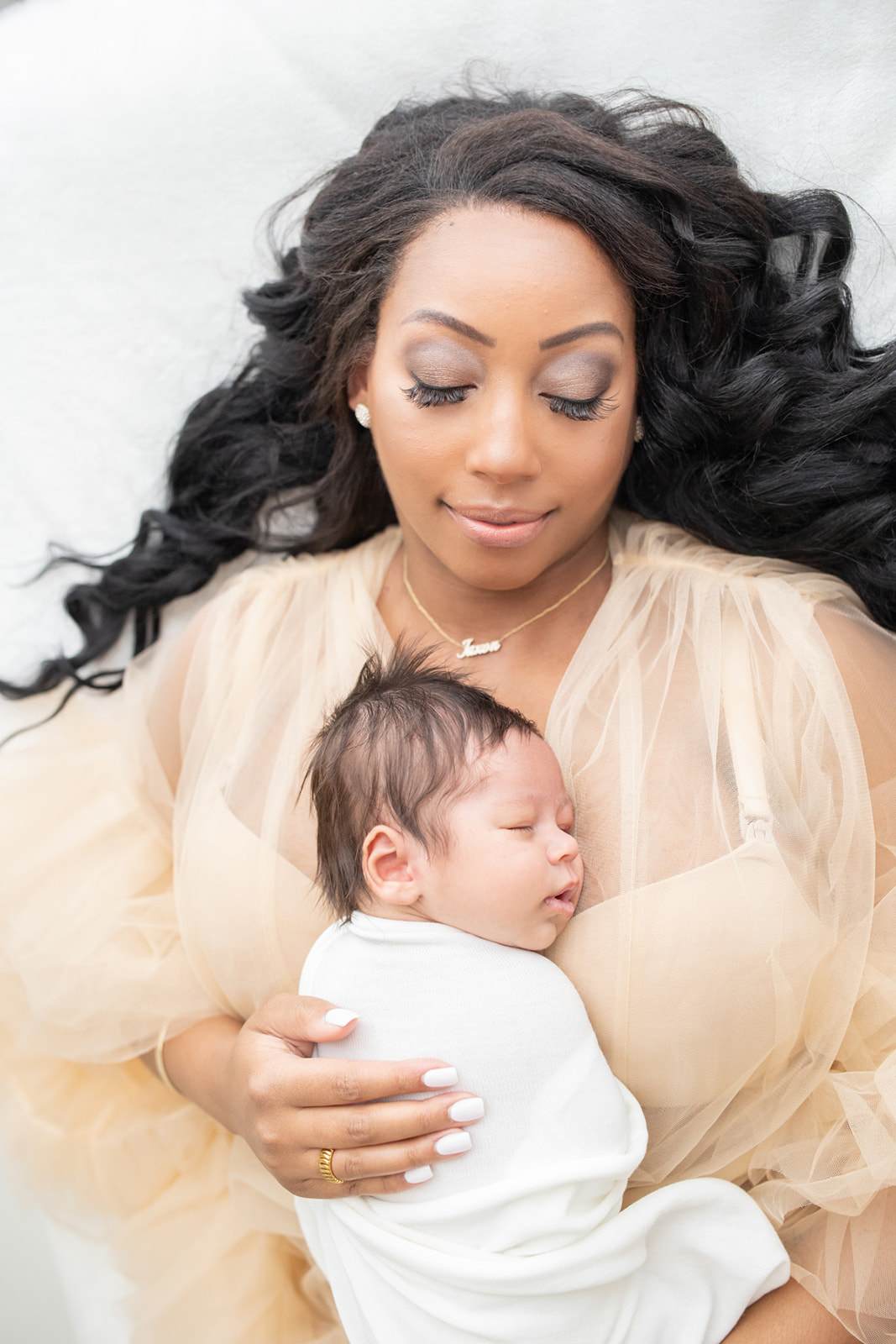 A mom to be lays on a bed in a beige dress with her newborn baby sleeping on her chest with help from a Postpartum Doula Pittsburgh