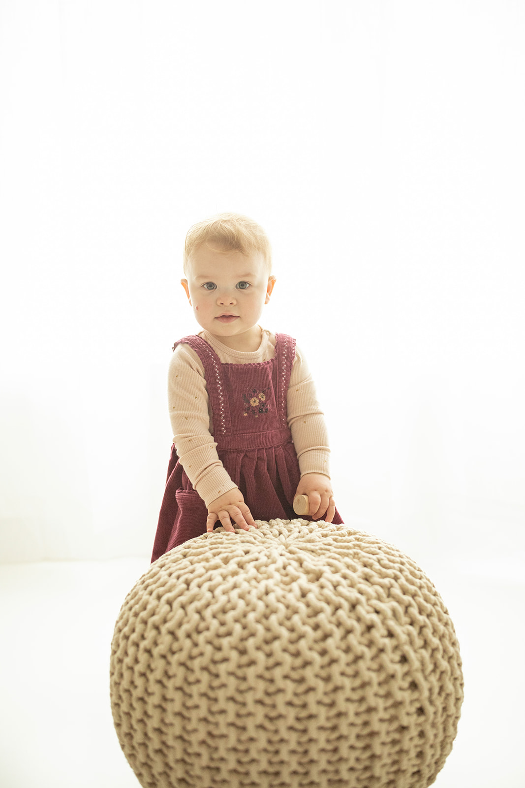 A young toddler stands in a purple dress in a studio with a woven ball