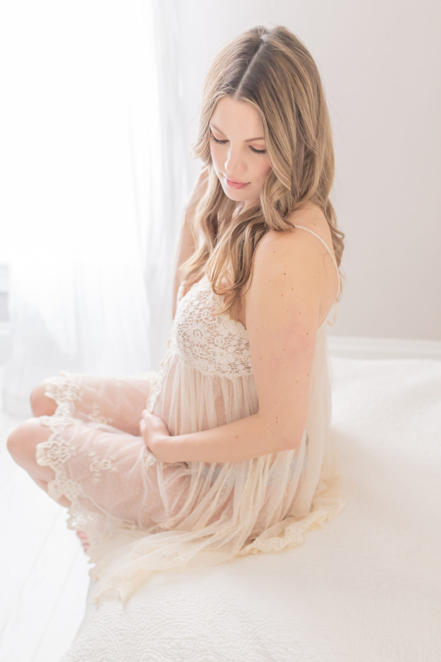 expecting mother sitting on edge of bed looking down and photographed by pittsburgh maternity photographer petite magnolia photography