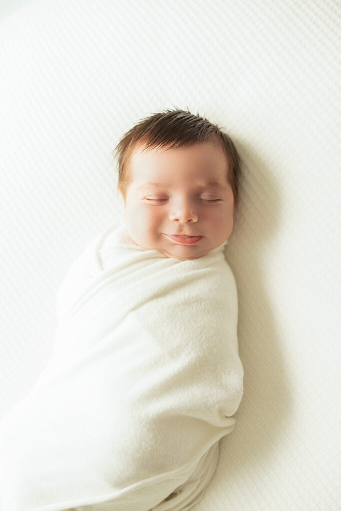 A newborn baby smiles in it's sleeps while in a white swaddle
