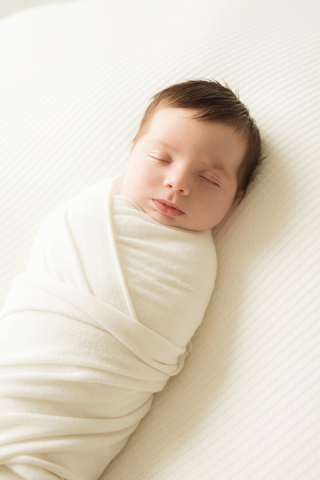 A newborn baby sleeps in a white swaddle on a matching bed in a studio for some Pittsburgh Newborn Photos