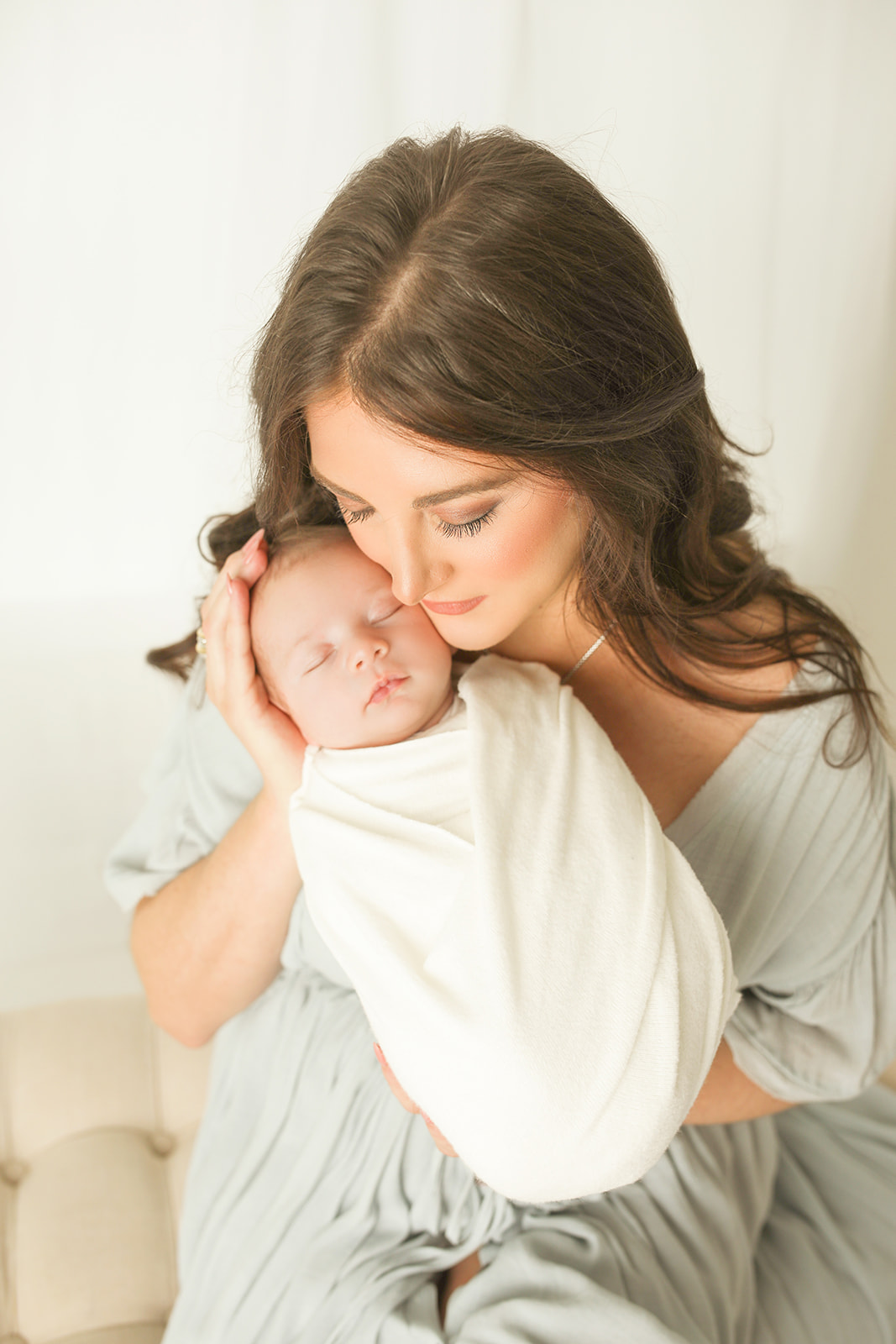 A new mother in a green dress snuggles her sleeping newborn baby while sitting on a bench