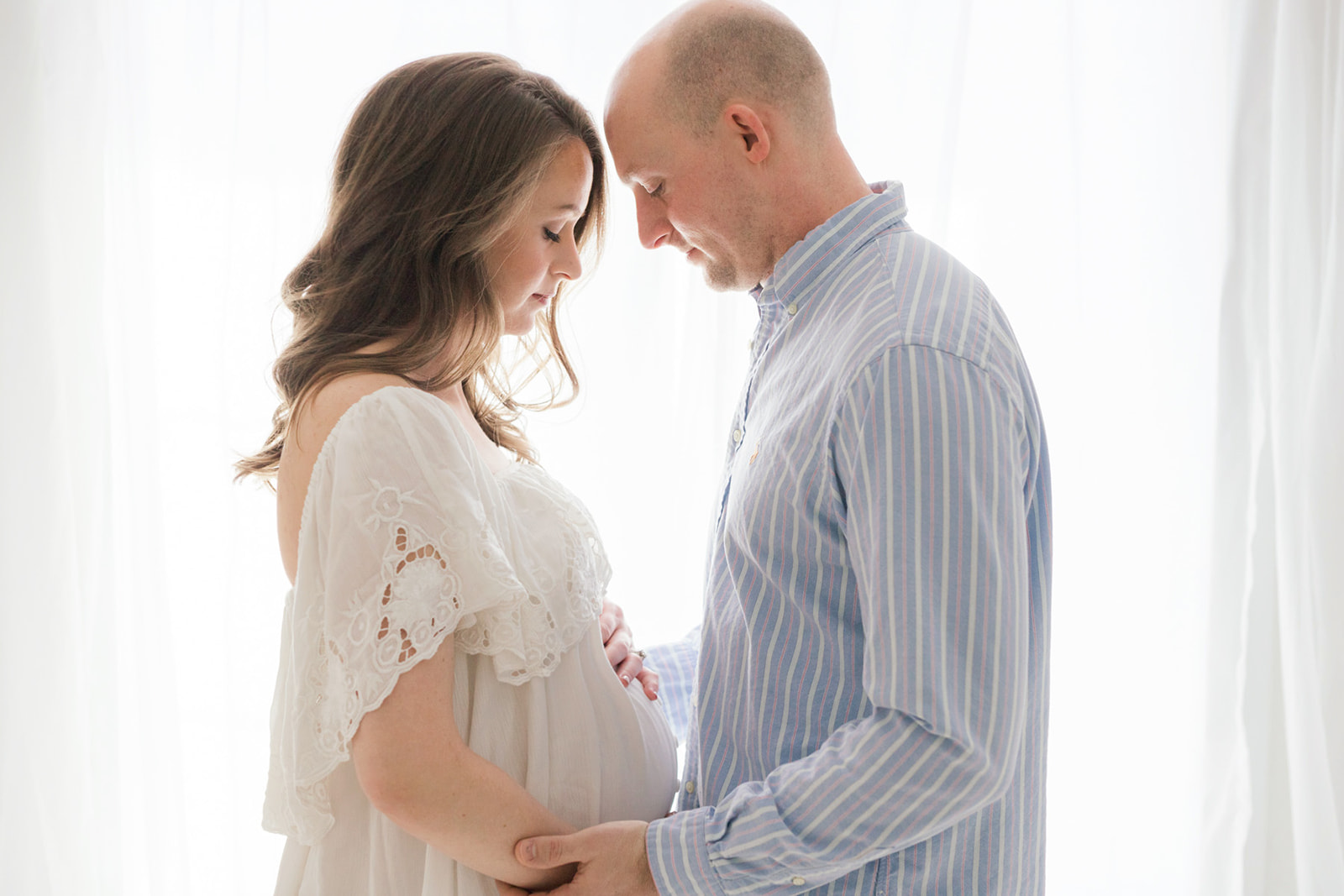 Happy expecting parents hold the bump while standing in the window of a studio after meeting Birthright Of Pittsburgh