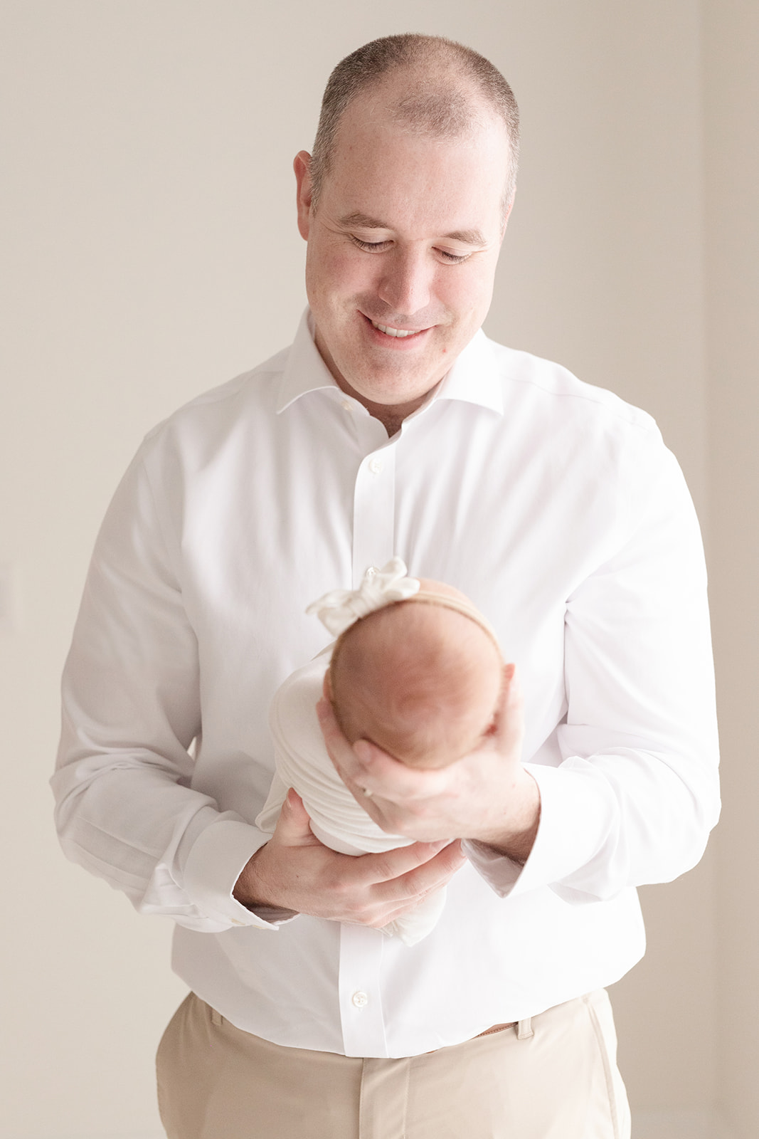 A happy father in a white shirt and khakis stands smiling down to his newborn daughter in his hands before meeting a Au Pair Pittsburgh