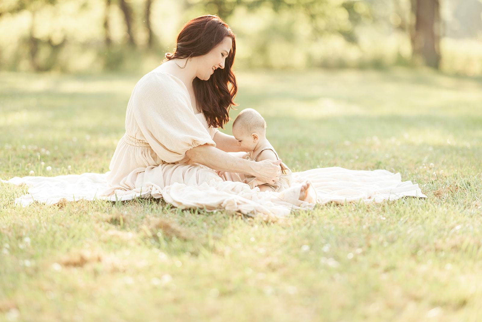 A happy mom plays with her infant in a park on a blanket at sunset after some baby music classes Pittsburgh