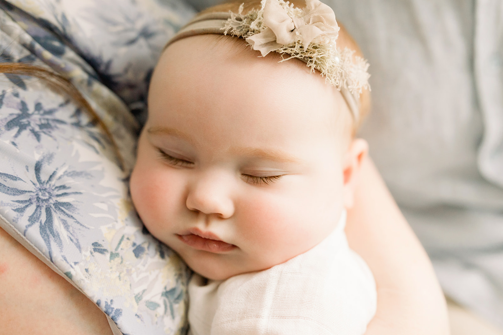 A newborn baby sleeps on mom's chest in a floral headband