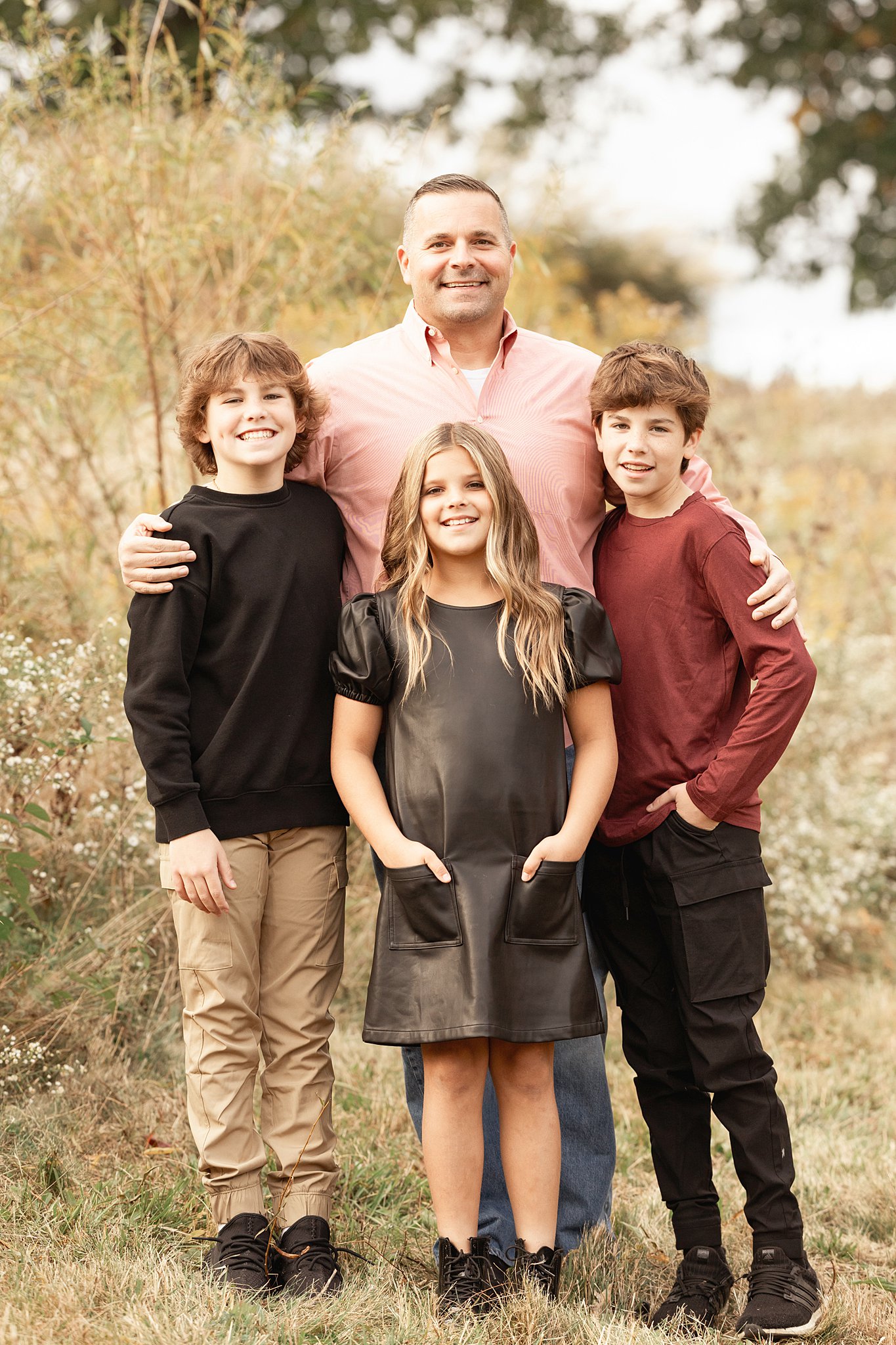 A happy dad hugs onto his two young sons and young daughter while standing in a park and staying at family friendly hotels pittsburgh