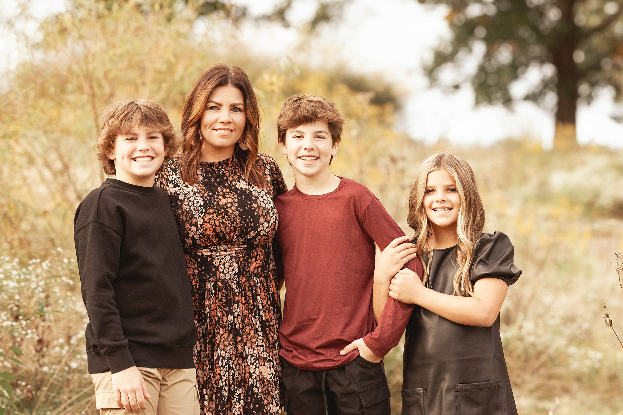 A mother stands in a park at sunset with her two sons and young daughter smiling with arms around each other while staying at family friendly hotels pittsburgh