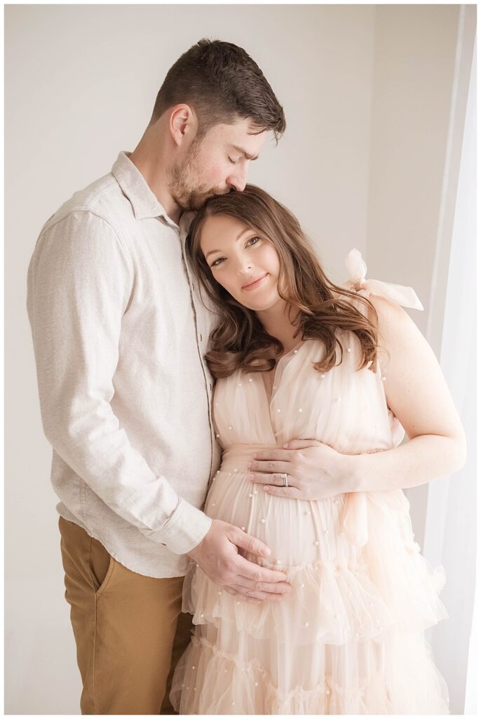 expecting mom in long dress with dad kissing her head