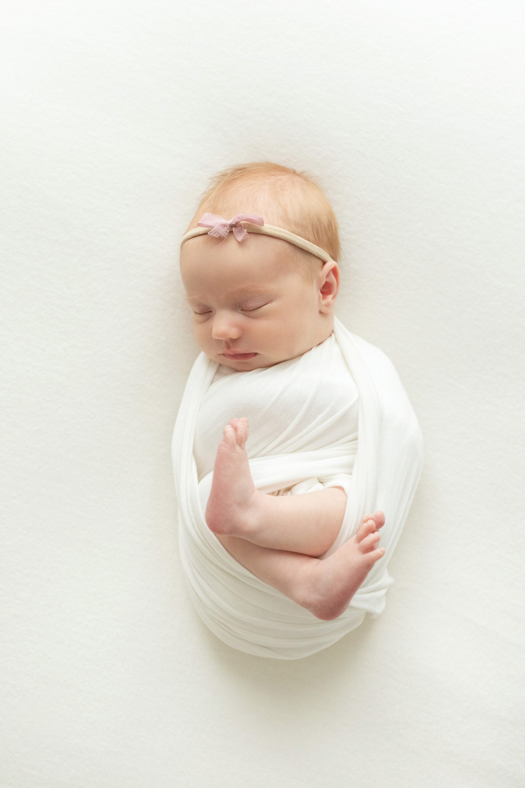 baby girl wrapped in ivory wrap with light pink bow headband