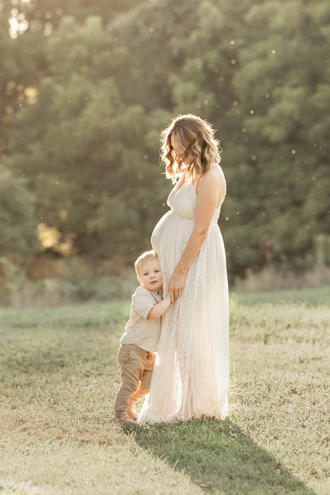 A toddler boy hugs his pregnant mother while standing in a field at sunset thanks to UPMC OBGYN