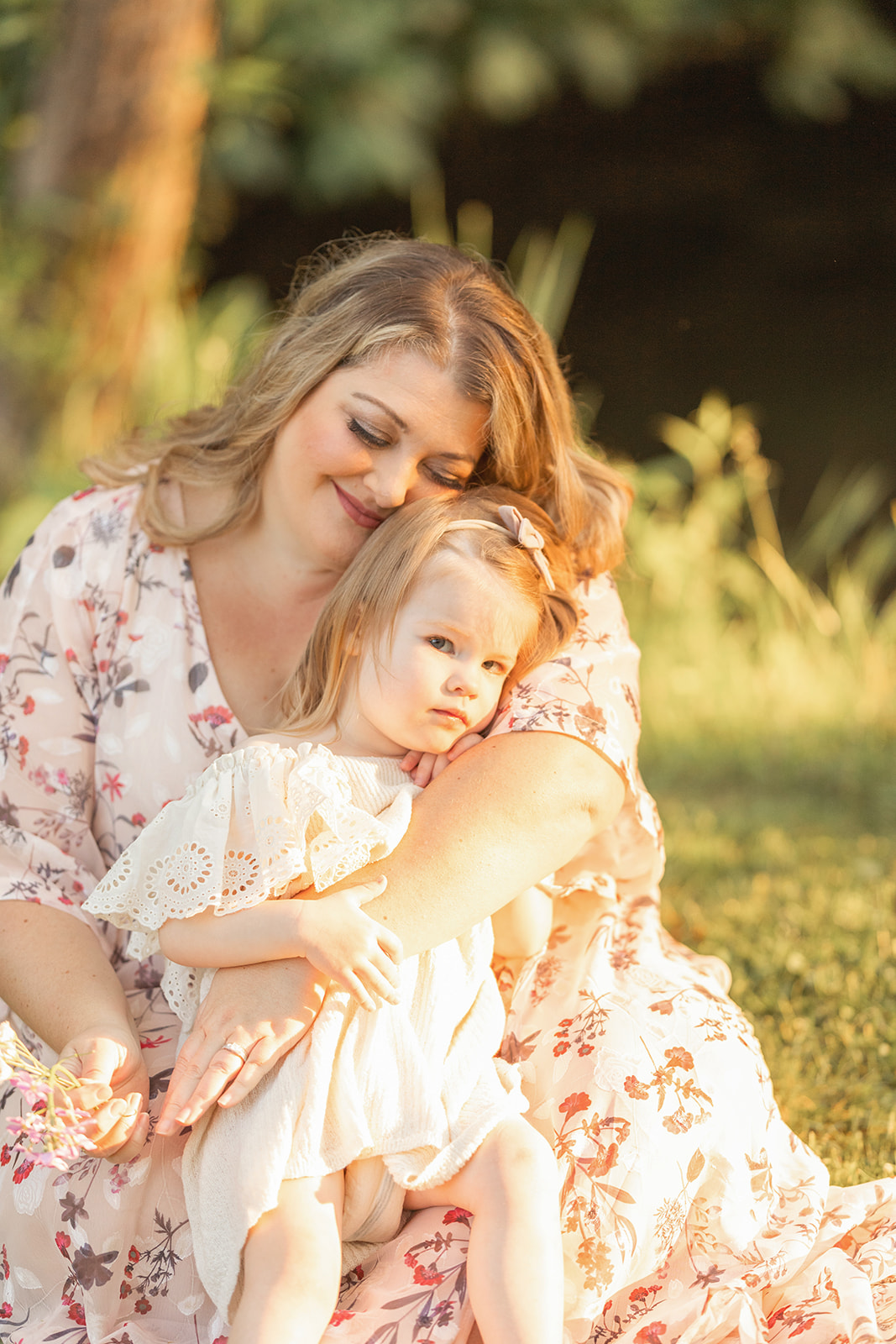 A happy mother snuggles her toddler daughter in her lap while sitting in a field at sunset before visiting Family-Friendly Restaurants Pittsburgh