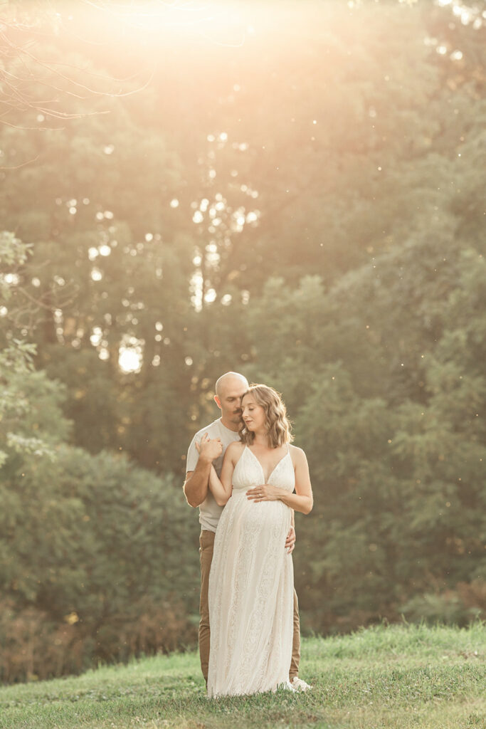 Expecting parents share an intimate moment in a park lawn at sunset while holding hands