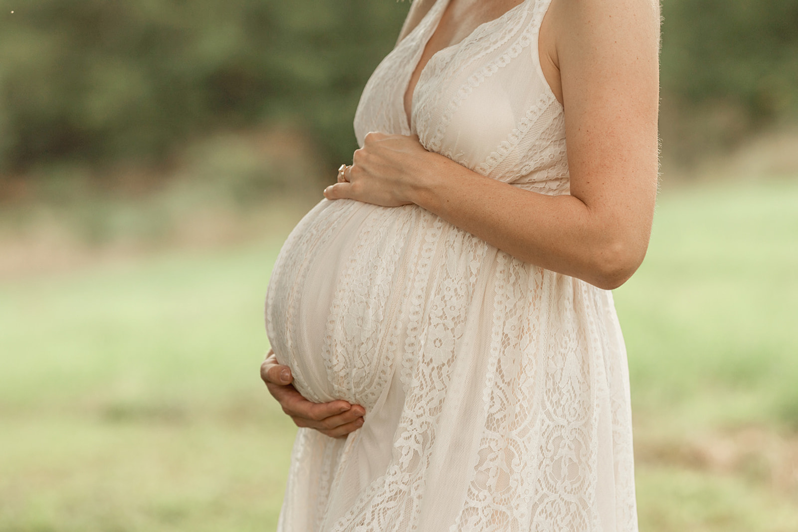 Details of a mother to be in a white lace dress holding her bump in a field after some Fertility Acupuncture Pittsburgh