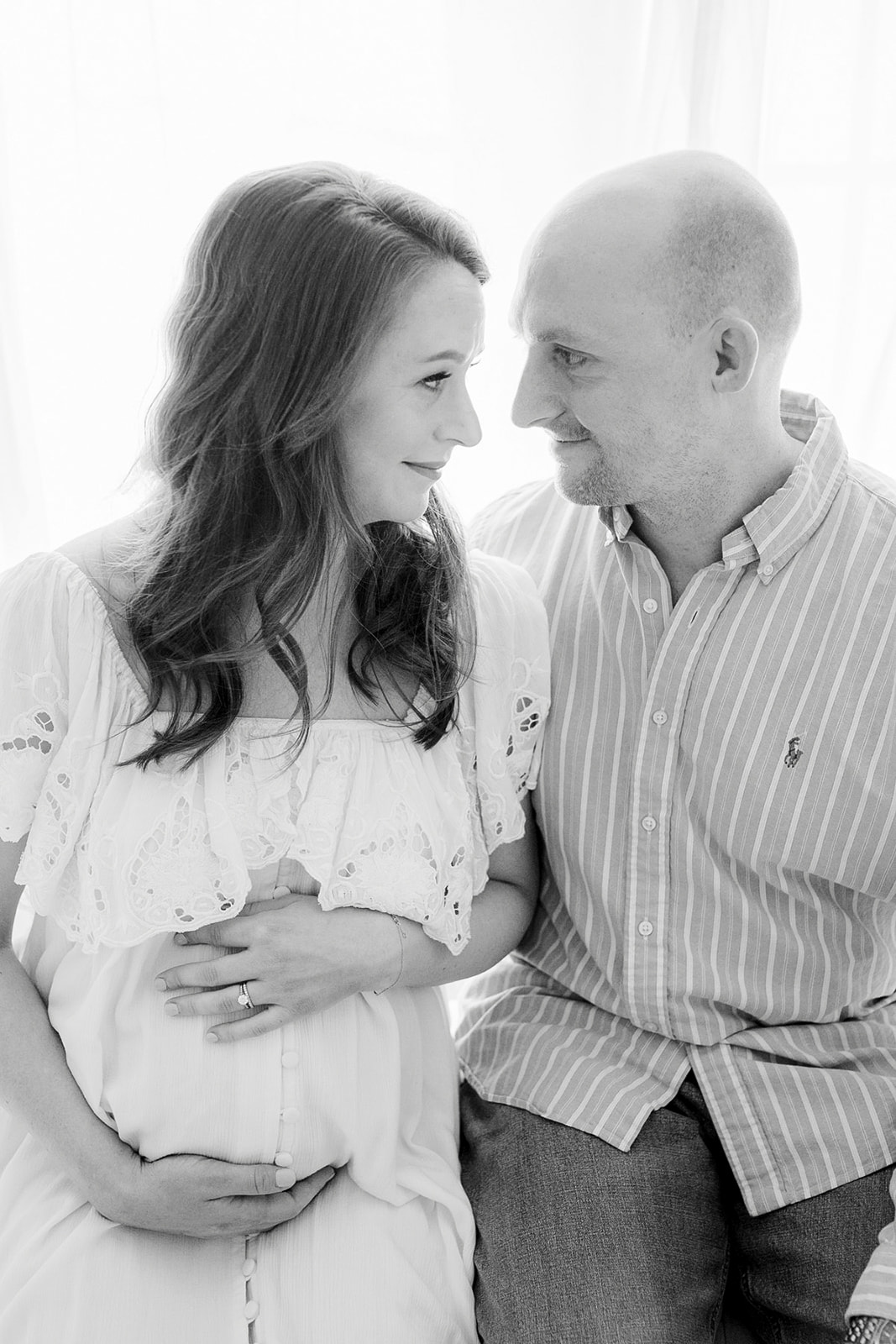 Happy expecting parents sit in a studio smiling at each other and holding the bump in black and white before exploring Pelvic Floor Therapy Pittsburgh